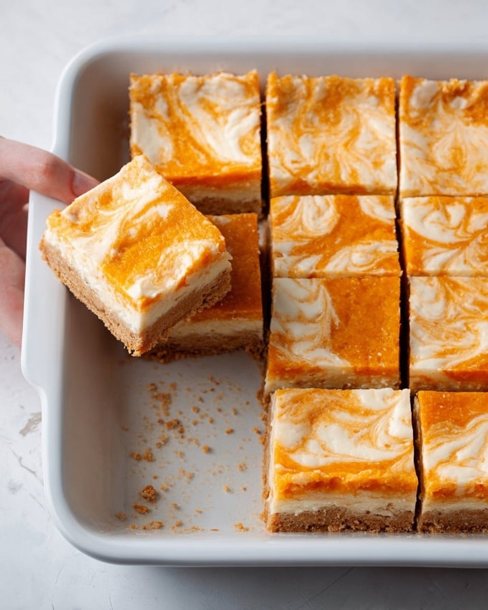 A white rectangular baking dish holds a batch of nine square dessert bars arranged in a grid. Each bar has three layers: a light brown crumbly base layer, a thick orange middle layer with a soft texture, and a pale cream-colored top layer with swirling patterns of orange mixed in. One bar is taken out from the dish and placed slightly to the side, showing the layers clearly. A woman's hand is gently holding one bar near the dish. The dish sits on a white marbled surface. photo taken with an iphone --ar 4:5 --v 7