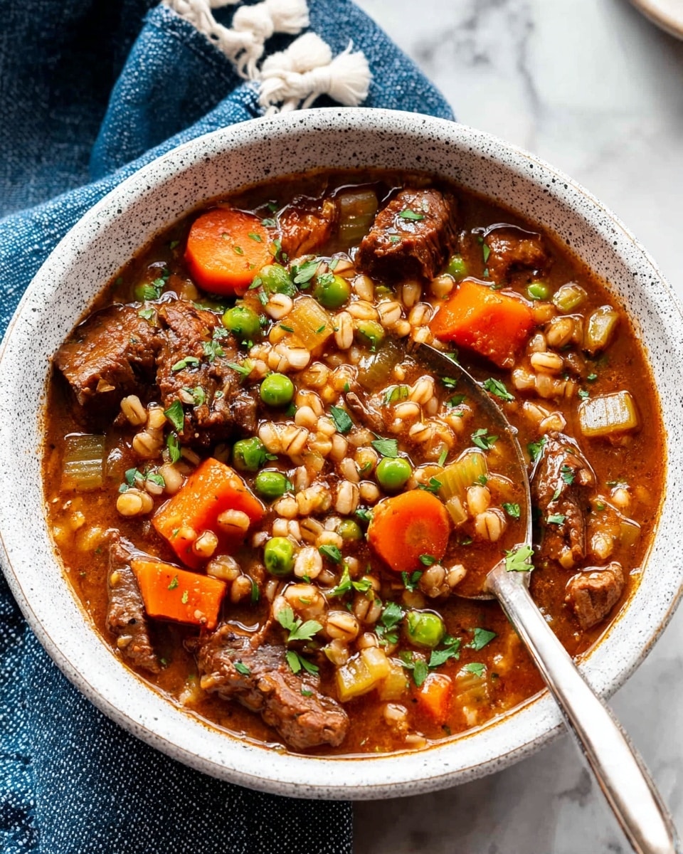 A white speckled bowl filled with three main layers: a clear brown broth as the base, chunks of dark brown tender meat scattered throughout, and bright orange carrot slices mixed with green peas and light beige barley grains floating on top. The soup is garnished with small green herbs evenly spread across the surface. A silver spoon rests inside the bowl, partially immersed in the soup. The bowl is placed on a white marbled surface with a blue cloth with white pom-poms on the left side. Another similar bowl with the same soup is blurred in the background. Photo taken with an iphone --ar 4:5 --v 7