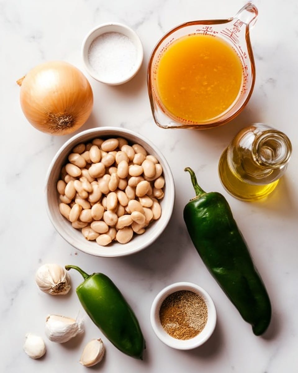 The image shows a flat lay of several uncooked ingredients arranged on a white marbled surface. In the center left, there is a white bowl filled with pale beige beans. Above the bowl to the left, there is a whole yellow onion, and next to it toward the top left corner is a small white bowl with salt. Below that, there is a bright green jalapeño pepper. To the right of the onion, a glass measuring cup contains orange-colored broth. Below this, near the center right, there is a dark green poblano pepper. Near the bottom right of the image, there is a small bottle of light golden oil, and to the left of that bottle is a small white bowl holding a mix of light brown spices. Toward the bottom left edge of the image, there are four garlic cloves and a whole lime placed near the middle bottom edge. The overall color tones include beige, green, orange, and white, all set on the smooth white marbled surface. Photo taken with an iphone --ar 4:5 --v 7