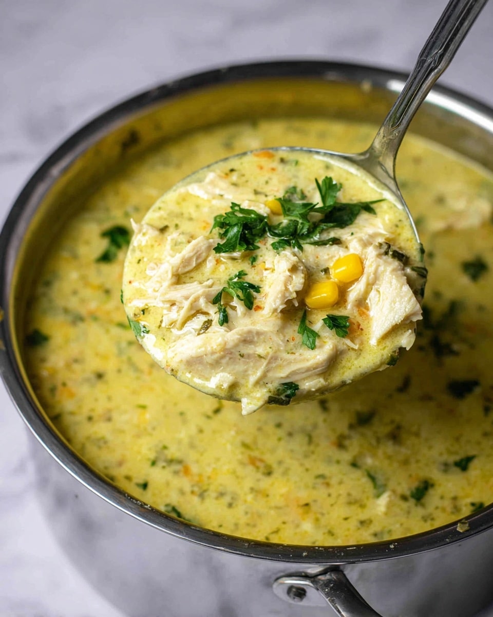 A close-up view of a thick, creamy yellow-green soup filled with small pieces of white chicken and scattered bits of corn, with fresh green parsley leaves sprinkled on top. A metal ladle is lifting a generous scoop of the soup from a stainless steel pot, showing its rich, chunky texture with chicken and vegetables clearly visible. The soup looks smooth with a slightly chunky texture, and the pot sits on a white marbled surface in soft, natural light, making the colors and textures stand out. photo taken with an iphone --ar 4:5 --v 7
