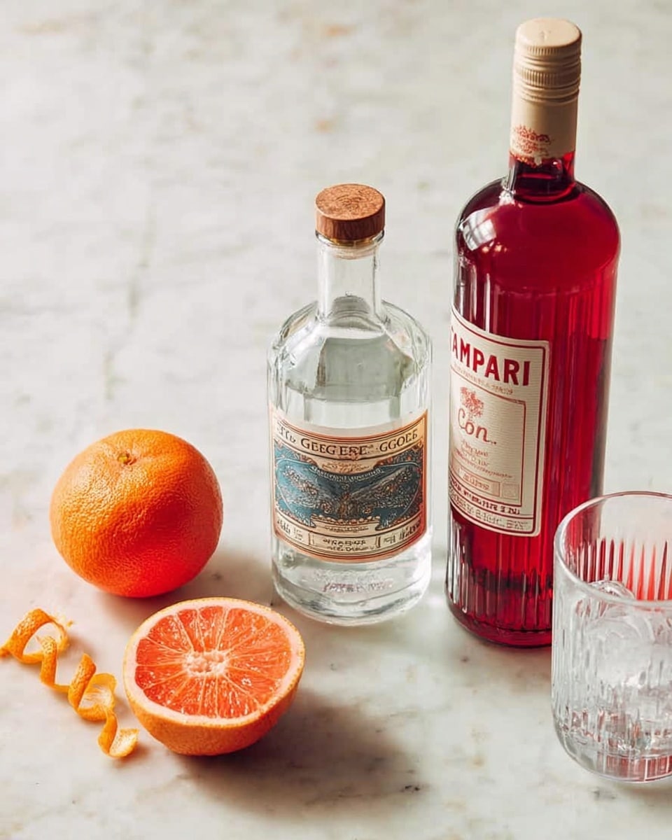The image shows a clear white marbled surface with a whole orange on the left side. Next to it, there is a twisted orange peel and a small piece of orange peel placed close by. In the center, there is a clear bottle of St. George gin with a cork stopper and a beige label. To the right, there is a tall red bottle of Campari with a beige cap and label. Behind the bottles, a clear empty drinking glass with a textured pattern is visible. Some ice cubes are seen faintly at the bottom right corner of the image. photo taken with an iphone --ar 4:5 --v 7