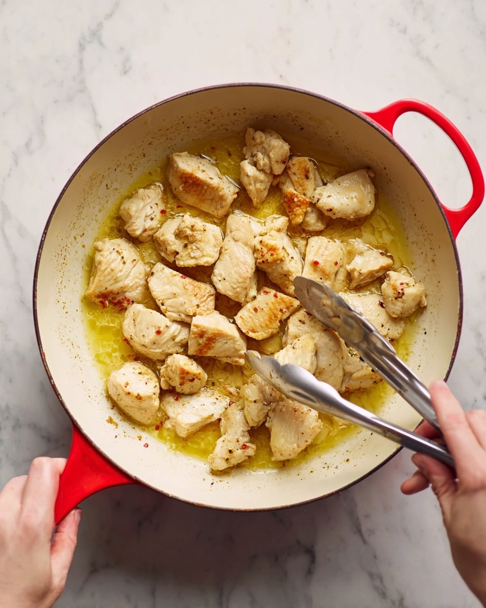 A white pot with red handles contains about twelve pieces of light golden cooked chicken pieces scattered unevenly in melted butter and juices that create a shiny, pale yellow layer at the bottom. A woman’s hand is holding the red handle of the pot on the left side, and another woman’s hand is holding silver tongs, lifting one piece of chicken on the right side. The surface under the pot is a white marbled texture. photo taken with an iphone --ar 4:5 --v 7