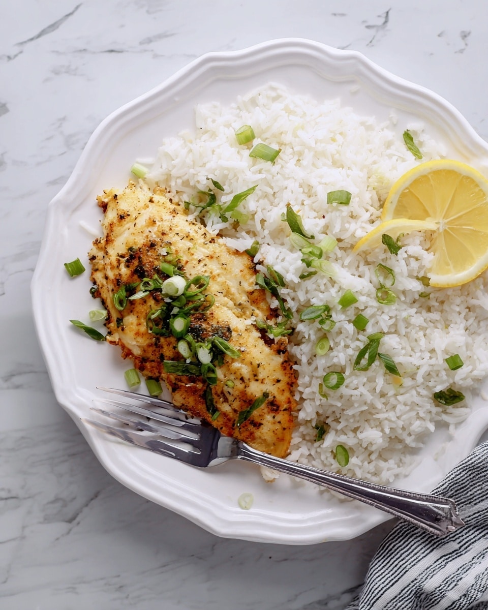 A white plate with scalloped edges holds a meal consisting of two layers: on the right side, a generous portion of fluffy white rice sprinkled with chopped green onions; on the left side, a golden brown seasoned chicken fillet topped with green onion pieces and a slightly crispy texture. A half lemon slice rests on the top right edge of the chicken and rice. A metal fork is placed on the bottom left edge of the chicken, and the plate is set on a white marbled surface with a striped cloth partially visible on the right side. Photo taken with an iphone --ar 4:5 --v 7