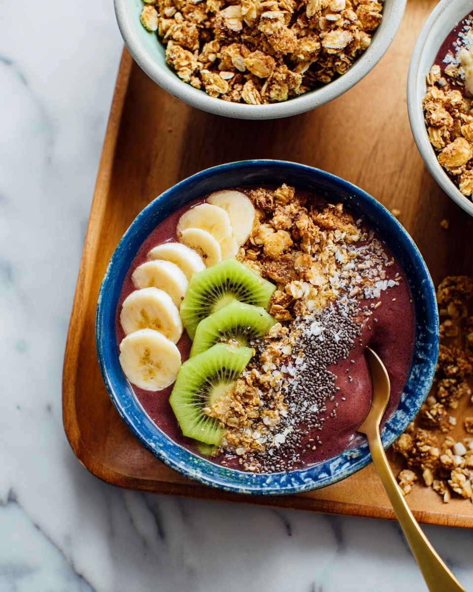 A blue bowl holds a smoothie bowl with three main layers: the base is a thick deep purple smoothie, topped with slices of light yellow banana arranged in the center, and bright green kiwi pieces placed beside the banana. One side of the bowl is covered with a crunchy golden-brown granola mixed with some chia seeds sprinkled on top. A gold spoon is dipping into the smoothie near the kiwi. The bowl sits on a wooden tray over a white marbled surface. Nearby, there are two other bowls partially shown, one with a similar smoothie topped with banana, kiwi, and granola, and another white bowl filled with more golden granola. photo taken with an iphone --ar 4:5 --v 7
