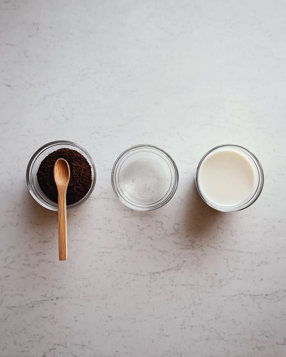 The image shows three small round containers placed side by side on a white marbled surface. On the left, there is a tiny wooden bowl filled with dark brown granules, resembling ground coffee or spices, and it has a small wooden spoon inside. In the middle, there is a clear glass bowl filled with transparent water. On the right, there is a clear glass bowl filled with creamy white milk. The arrangement is simple and neat, with the bowls evenly spaced. photo taken with an iphone --ar 4:5 --v 7
