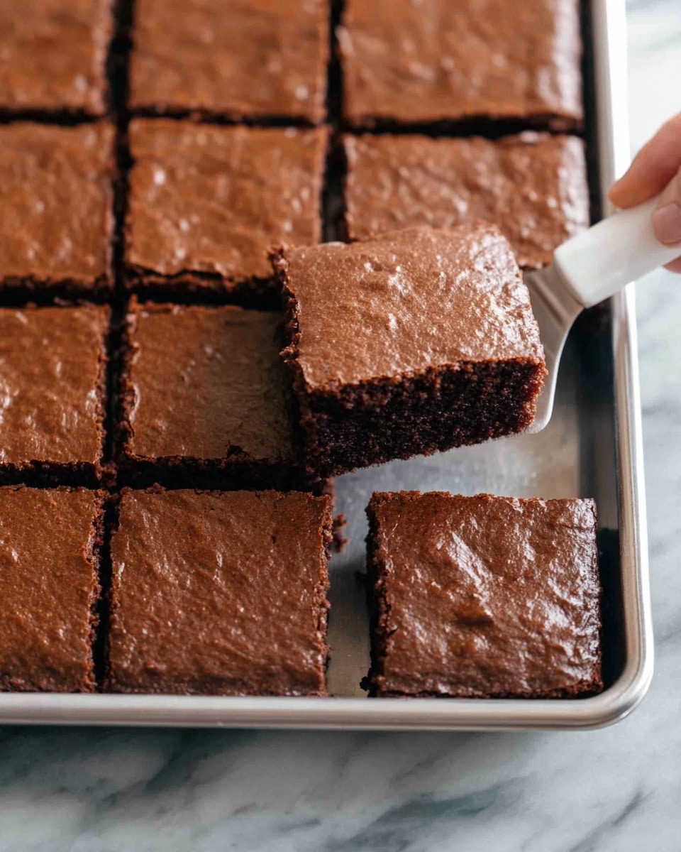A close-up view of a tray of chocolate brownies, cut into square pieces with clear edges. Each brownie has one layer, showing a moist and slightly crumbly dark brown inside with a thin, smooth, and slightly shiny crust on top. A woman’s hand is lifting one brownie square out of the tray with a white-handled metal spatula. The tray is silver and sits on a surface with a white marbled texture. Photo taken with an iphone --ar 4:5 --v 7