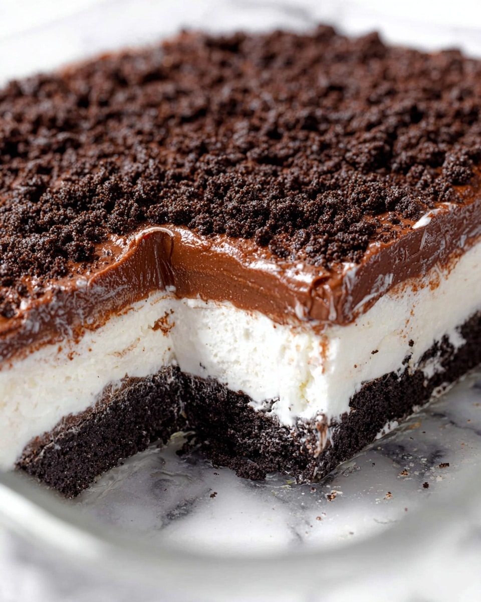 This is a close-up image of a dessert with four visible layers in a clear glass dish. The bottom layer is a dark, crumbly cookie crust, followed by a thick, white creamy layer. Above the cream is a smooth, shiny chocolate layer, and topped with another white creamy layer slightly thinner than the one below the chocolate. The top is covered with a thick, rough layer of crushed dark chocolate cookies. The dish is placed on a white marbled surface. Photo taken with an iphone --ar 4:5 --v 7