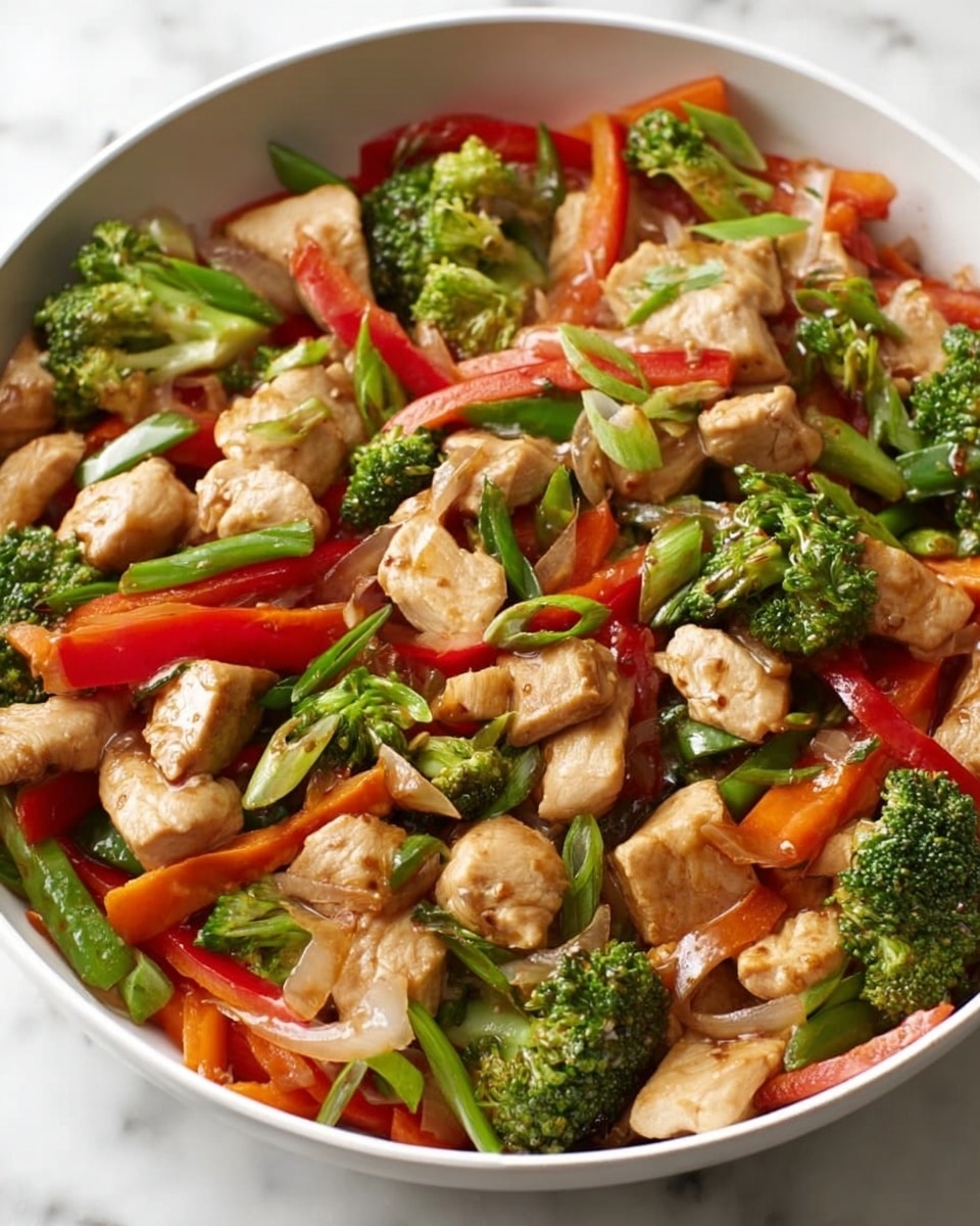 A close-up view of a stir-fry dish in a white bowl showing three main layers: small, light brown pieces of cooked chicken scattered evenly; bright green broccoli florets and sliced green onions mixed throughout; and thin, vibrant red bell pepper strips and orange carrot slices spread around. The chicken pieces look tender, surrounded by shiny, slightly oily vegetables with a fresh and colorful look, all placed on a white marbled surface. Photo taken with an iphone --ar 4:5 --v 7