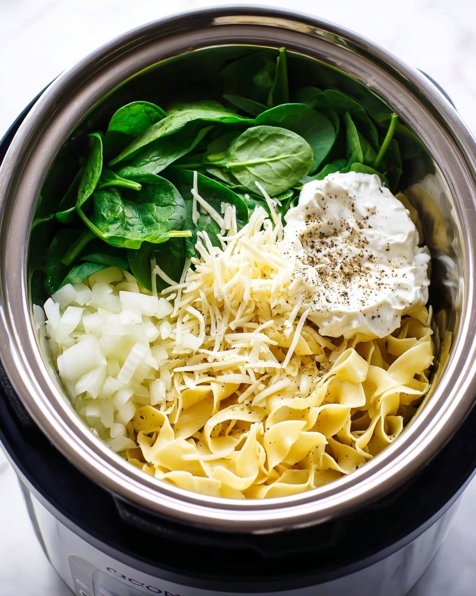 The image shows a slow cooker filled with several fresh ingredients arranged in layers. At the bottom right, there are pale yellow egg noodles with a soft, curly texture. Next to the noodles, there is a small pile of shredded white cheese sprinkled lightly with ground black pepper. To the right of the cheese, there is a dollop of white sour cream also topped with black pepper. Toward the left side, there are fresh, bright green spinach leaves with a smooth texture. At the far left, finely diced white onions complete the arrangement. The ingredients sit inside a shiny silver and black slow cooker, all on a white marbled surface. Photo taken with an iphone --ar 4:5 --v 7