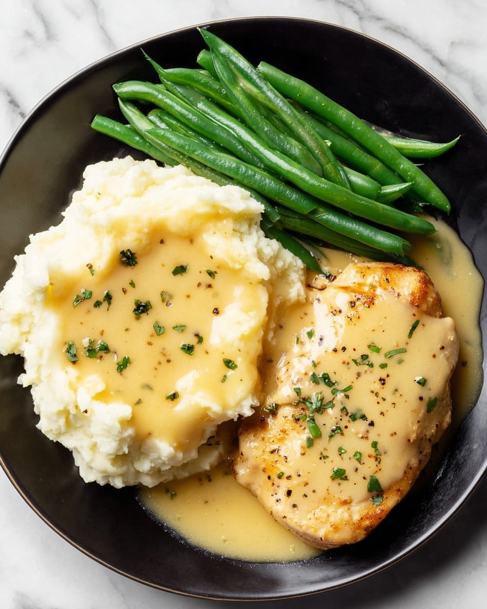 A black plate holds three main parts: on the left, there is a fluffy mound of white mashed potatoes with a smooth, creamy yellow gravy poured over the top, sprinkled with small green herb pieces and black pepper; on the top side of the plate, a neat stack of bright green cooked green beans rests, showing a shiny texture; on the right, a single piece of golden brown cooked chicken is covered by the same creamy yellow gravy with scattered green herbs on it. The plate sits on a white marbled surface photo taken with an iphone --ar 4:5 --v 7