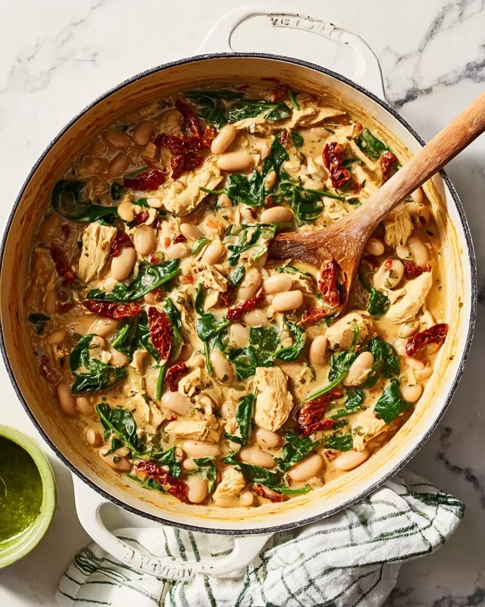 A white skillet filled with layers of food, starting with a base of small white beans, mixed with green spinach leaves and sun-dried tomato pieces. There are light tan artichoke hearts scattered through the mix, all coated in a creamy light brown sauce. A wooden spoon is partly dipped in the dish, resting inside the skillet. The skillet sits on a white marbled surface, with a green and white checkered cloth nearby and a glass of green sauce beside it. photo taken with an iphone --ar 4:5 --v 7