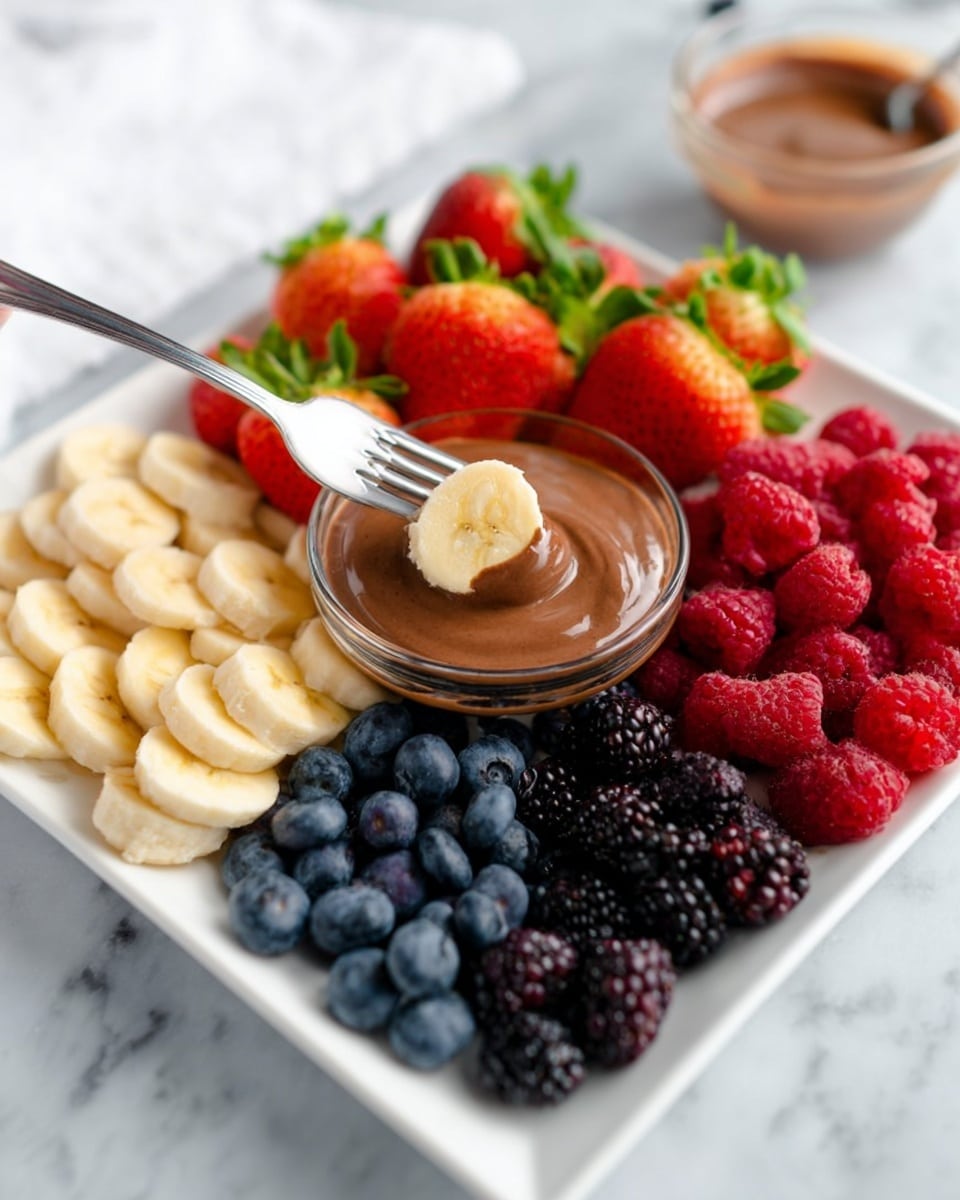 A white square plate holds a colorful arrangement of fresh fruits and a small glass bowl of smooth, chocolate-colored dip in the center. The plate is divided into five sections: fresh green-topped strawberries on the left, thick pale yellow banana slices on the bottom left and back right, deep blue blueberries on the bottom right, bright red raspberries on the right, and dark purple-black blackberries on the back left. A woman’s hand is holding a fork with a banana slice dipped halfway in the chocolate dip above the bowl. The plate sits on a white marbled surface, with a small glass bowl of the same chocolate dip blurred in the background. Photo taken with an iphone --ar 4:5 --v 7