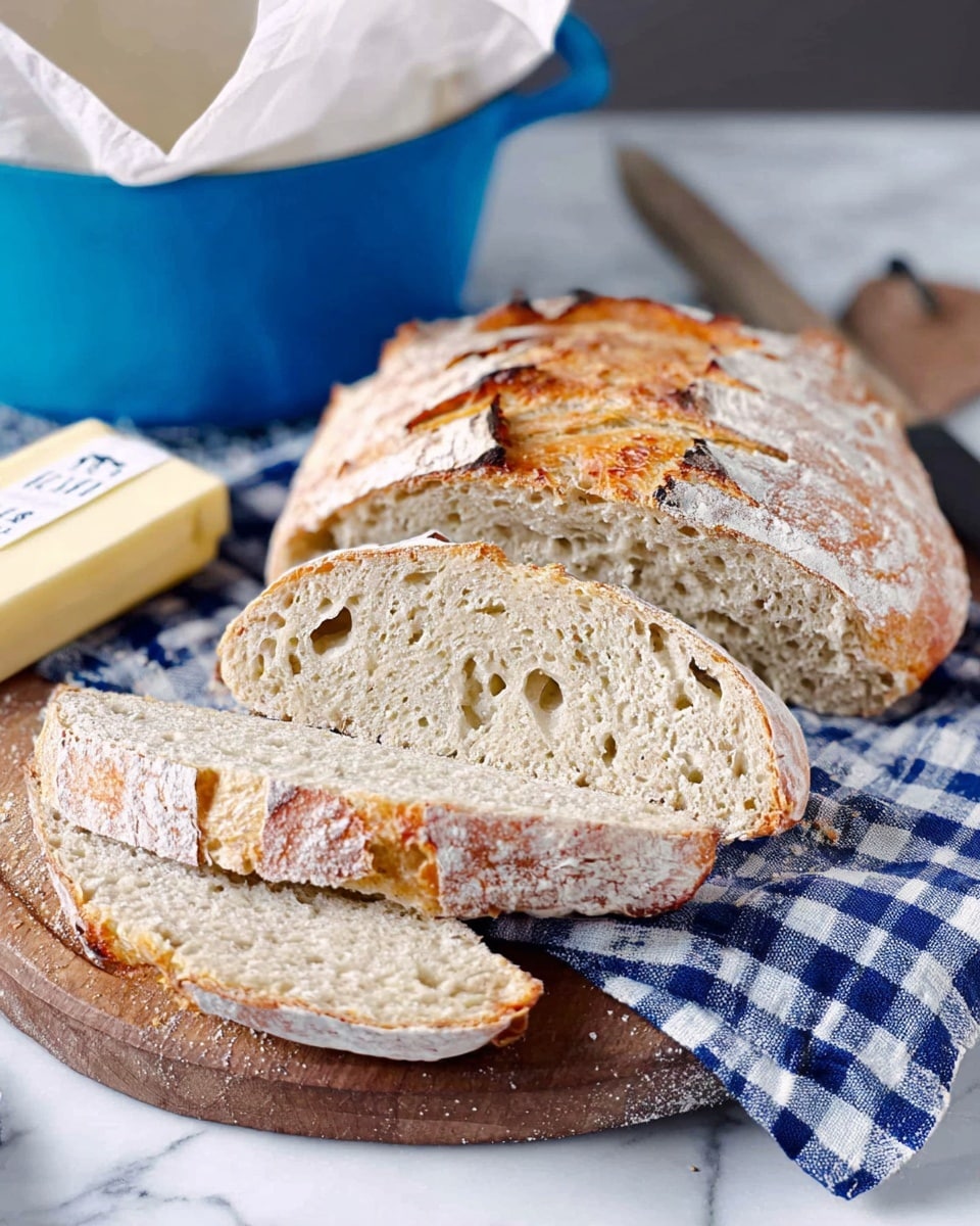 The image shows a loaf of rustic bread sliced into five thick pieces, placed on a wooden board. The bread has a golden-brown crust with a slightly cracked surface, and the inside is light beige with a soft, airy texture full of small holes. The board rests on a blue and white checkered cloth, which is set on a white marbled surface. To the left of the bread is a stick of butter partially wrapped in white paper with some text visible. In the background, there is a white bowl with a bright blue exterior, lined with parchment paper. Photo taken with an iphone --ar 4:5 --v 7