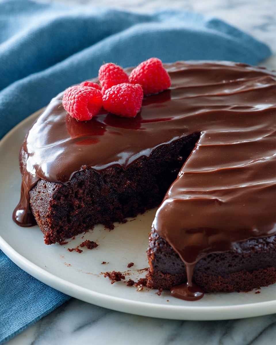 The image shows a two-layer chocolate cake on a white plate, the bottom layer is a dark, rich chocolate cake with a soft, crumbly texture, while the top layer is a thick, glossy chocolate glaze smoothly spread over the cake with gentle waves. Three bright red raspberries are placed on the top left side of the cake, adding a fresh pop of color. A slice is removed from the cake, revealing the shiny chocolate glaze dripping slightly over the moist cake inside. The plate sits on a white marbled surface with a soft blue cloth nearby. Photo taken with an iphone --ar 4:5 --v 7