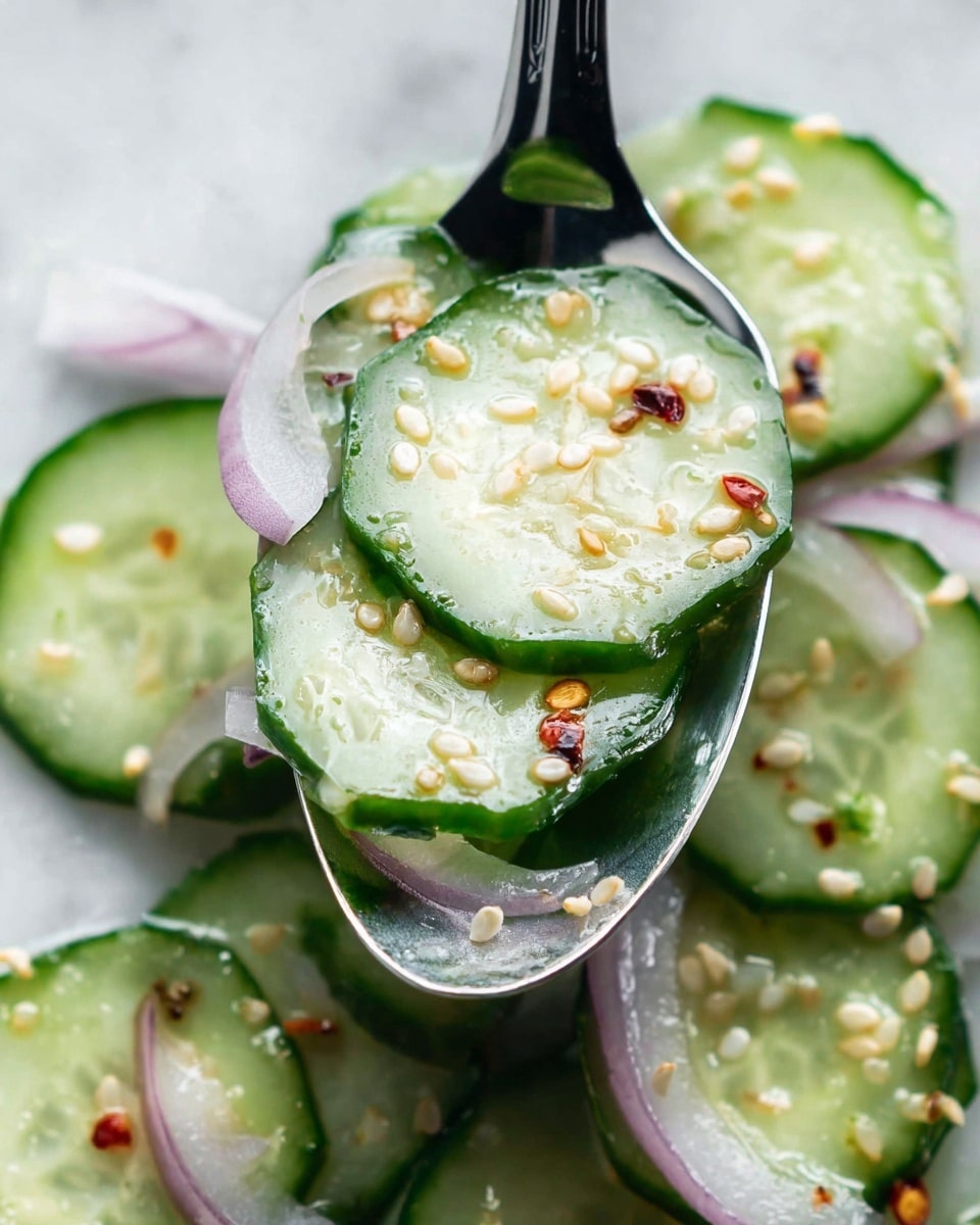 The image shows a close-up of a spoon holding several thin cucumber slices, light green with dark green edges, layered on top of each other. There are thin slices of pale purple onion mixed with the cucumbers. The cucumbers and onions are sprinkled with small white sesame seeds and tiny red chili flakes, creating a textured look on the fresh, shiny cucumber surface. The spoon rests on a white marbled surface with more cucumber and onion slices scattered around. The photo captured highlights the freshness and crispness of the vegetables with a bright and light background. Photo taken with an iphone --ar 4:5 --v 7