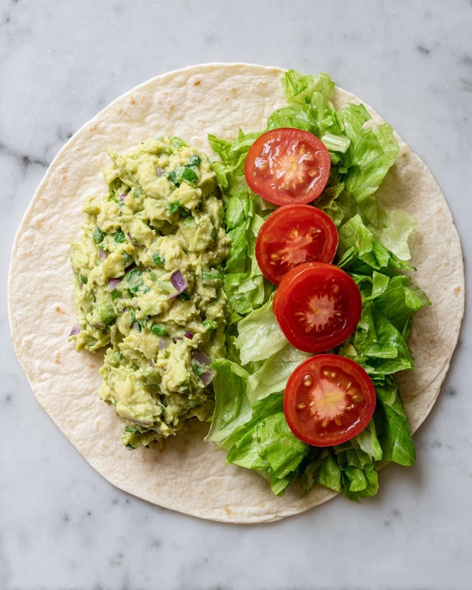 A soft, round tortilla lays flat on a white marbled surface with three main layers on top. On the left side, there is a chunky mix of green avocado mash with small bits of purple onion and herbs, giving a textured, creamy look. To the right, there are bright green, leafy lettuce pieces that appear fresh and crisp. On top of the lettuce, three round, red tomato slices are evenly spaced, showing their juicy interiors. The colors contrast nicely with the light beige tortilla under them. Photo taken with an iphone --ar 4:5 --v 7
