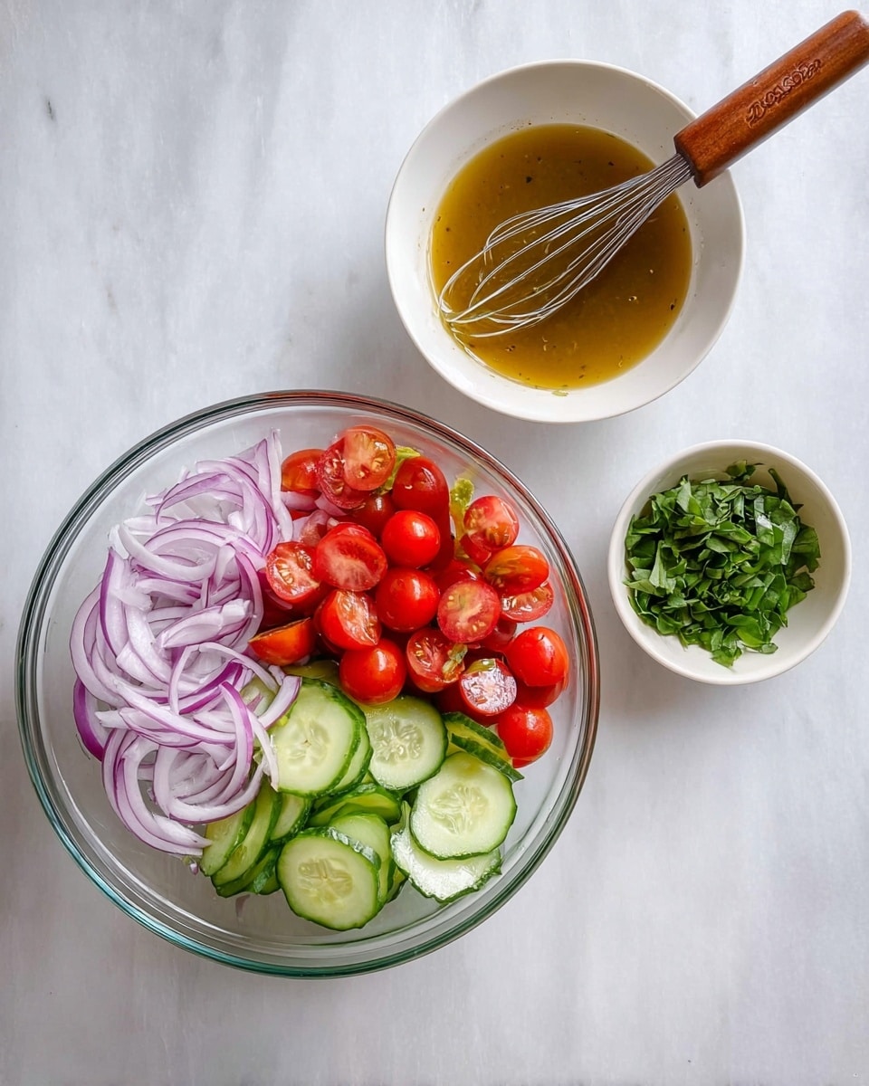 A clear glass bowl filled with three layers of fresh vegetables arranged side by side: thin light purple onion rings on the left, bright red cherry tomatoes halved in the middle, and curved slices of green cucumber with pale flesh on the right. Above the bowl, a white bowl contains a golden brown dressing with a wooden-handled whisk resting inside. Next to the dressing bowl is a smaller white bowl with bright green leafy herbs. All items are placed on a white marbled surface. photo taken with an iphone --ar 4:5 --v 7