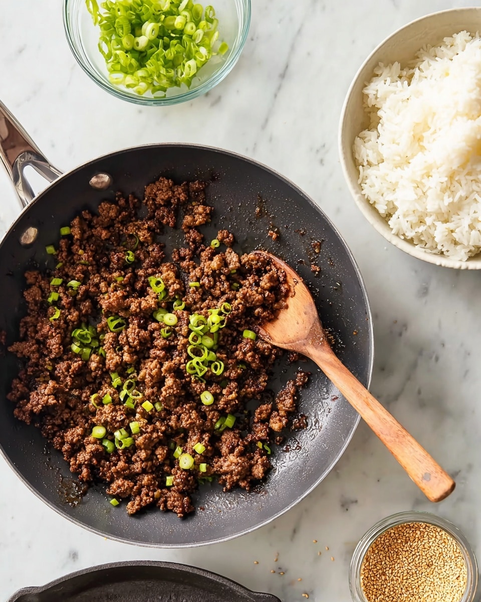 A black frying pan filled with cooked ground meat that is dark brown and slightly crispy in texture, sprinkled with small green sliced spring onions on top. A wooden spoon with a light brown handle rests inside the pan on the right side, touching the meat. Above the pan is a white bowl full of plain white cooked rice, showing soft and fluffy texture. To the left of the pan is a small clear glass bowl containing more sliced green spring onions. Below the pan is a dark gray cast iron skillet, empty and clean. To the lower right of the pan is a small clear glass container with golden toasted sesame seeds, some scattered lightly on the white marbled surface around it. The entire scene is set on a white marbled table. photo taken with an iphone --ar 4:5 --v 7