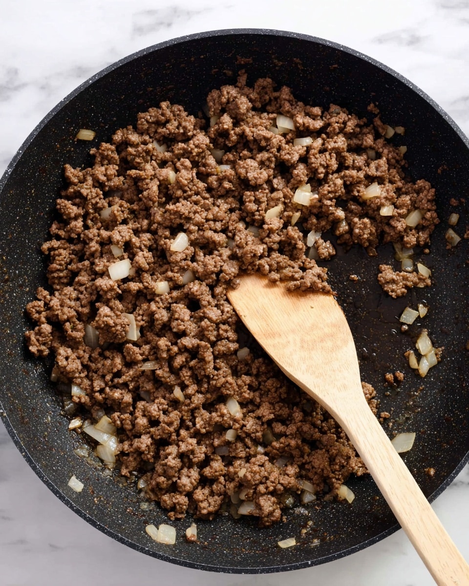 A black pan filled with cooked ground meat mixed with small pieces of lightly cooked onions is shown on a white marbled surface. The cooked meat is brown with a crumbly texture, and the onions add slightly translucent white bits scattered throughout. A wooden spoon with a smooth light brown handle is placed in the pan, stirring the mixture. The pan has a shiny, slightly oily surface, showing some small spots of cooked residue. Photo taken with an iphone --ar 4:5 --v 7