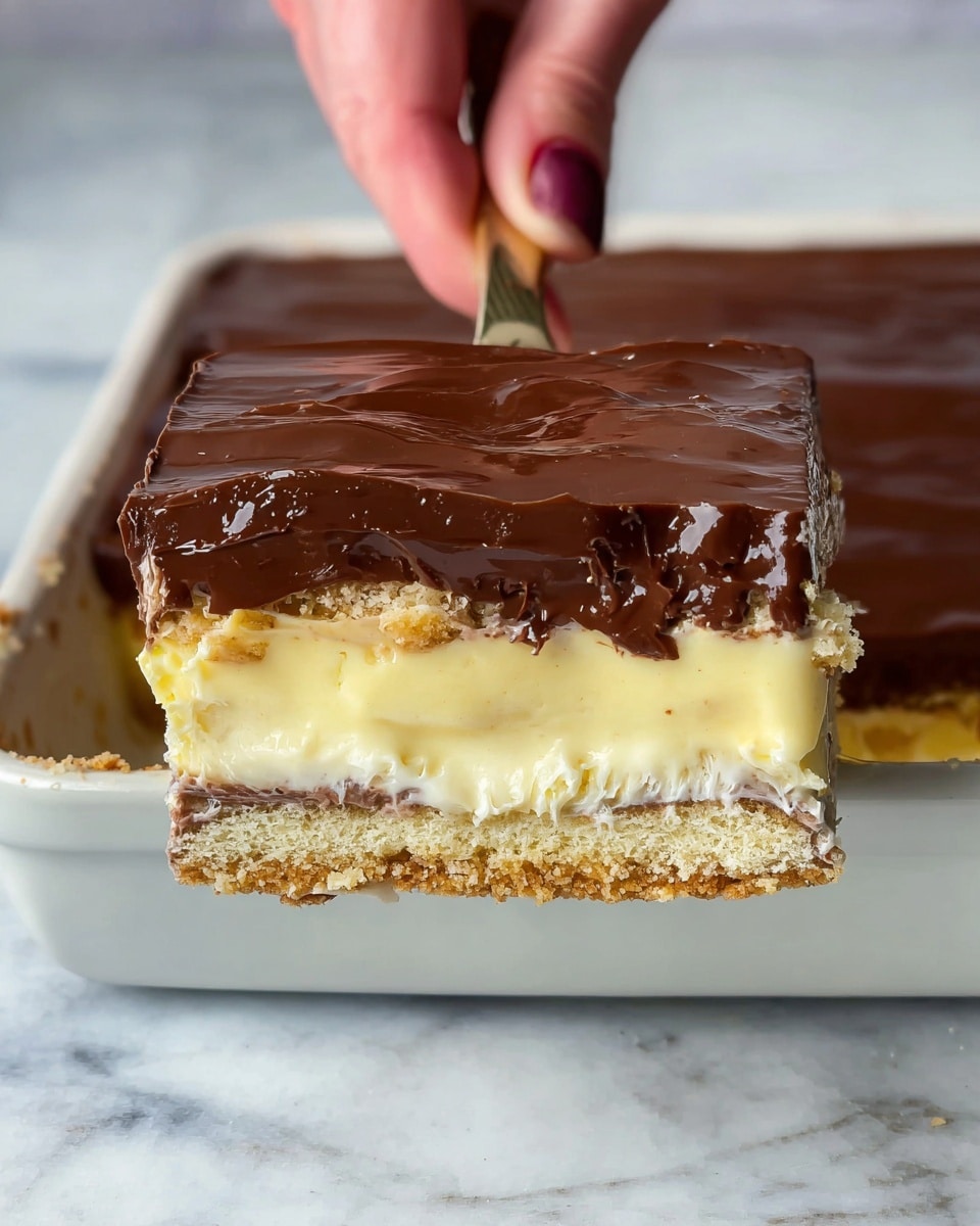 The image shows a close-up of a square slice of dessert being lifted by a woman's hand using a spatula. The dessert has four visible layers: the top layer is a smooth, dark brown chocolate glaze; underneath is a crumbly, golden brown biscuit layer; below this is a thick, creamy, pale yellow custard with small bits of biscuit mixed inside; the bottom layer is another golden brown biscuit base. The dessert rests in a white ceramic dish on a white marbled surface. The chocolate glaze is shiny and evenly spread, while the custard layer looks soft and fluffy. Photo taken with an iphone --ar 4:5 --v 7
