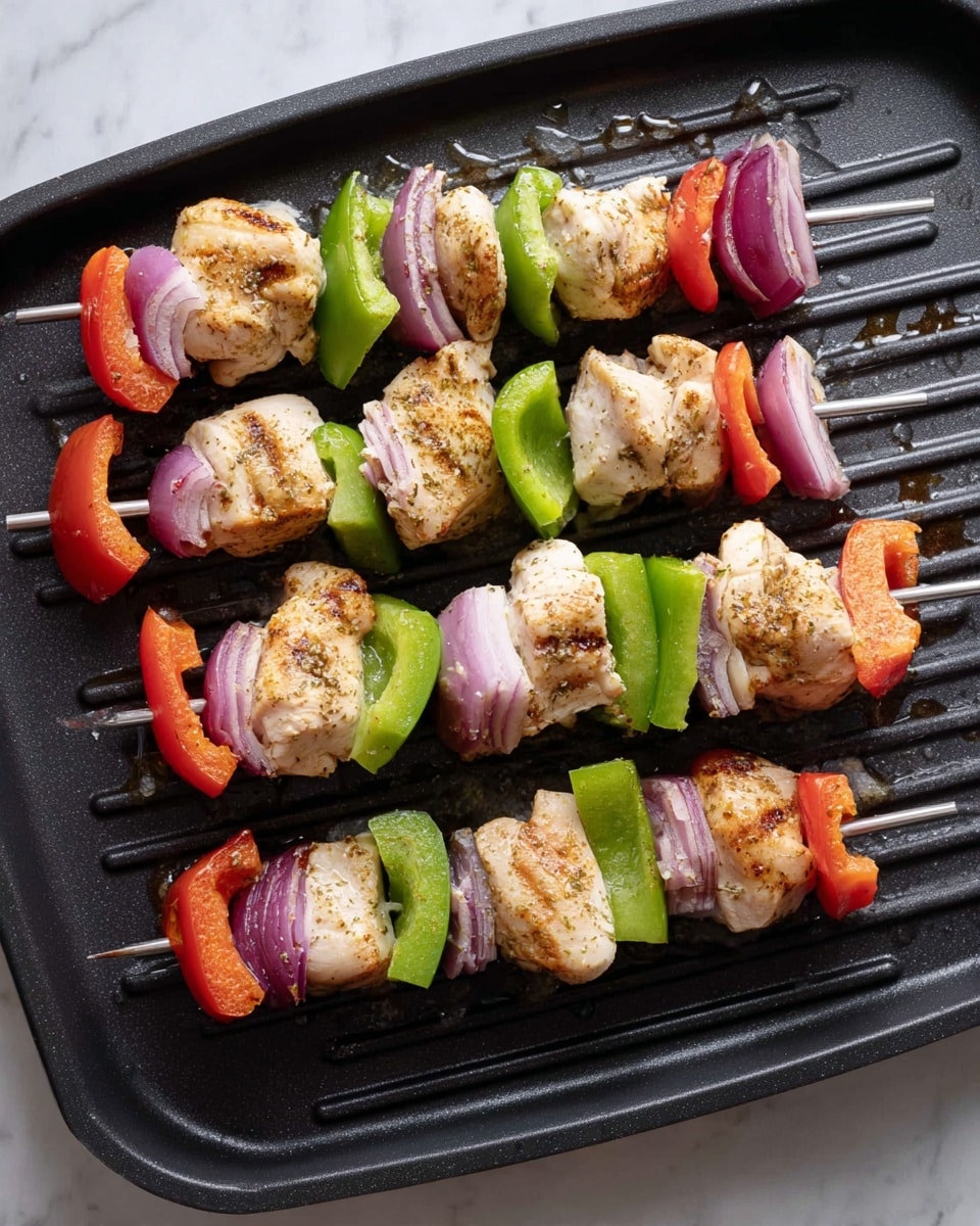 There are six skewers placed on a black grill pan on a white marbled surface. Each skewer has three layers of food with colors and textures from bottom to top: white chicken pieces with a light golden seasoning, bright green bell pepper chunks with a smooth surface, and a mix of red bell pepper and purple onion pieces with a slightly shiny texture. The chicken pieces are thick and irregularly shaped, the green bell peppers are cut into rectangular blocks, and the onions are in curved segments. The grill pan has droplets of oil or water on its surface. photo taken with an iphone --ar 4:5 --v 7