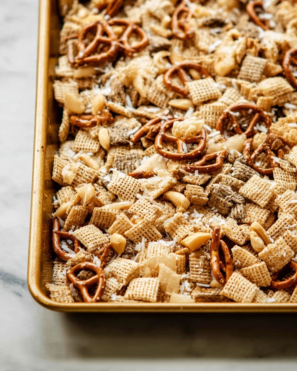 The image shows a close-up of a baking tray filled with a snack mix made of several layers of light beige square cereal pieces, dark brown twisted pretzels, and light tan mixed nuts. The texture looks crunchy, with some cereal pieces having a woven pattern and the pretzels showing their twisted shape. There are also small white coconut flakes sprinkled on top, adding a slight rough texture. The tray has a golden metallic color and rests on a white marbled surface photo taken with an iphone --ar 4:5 --v 7
