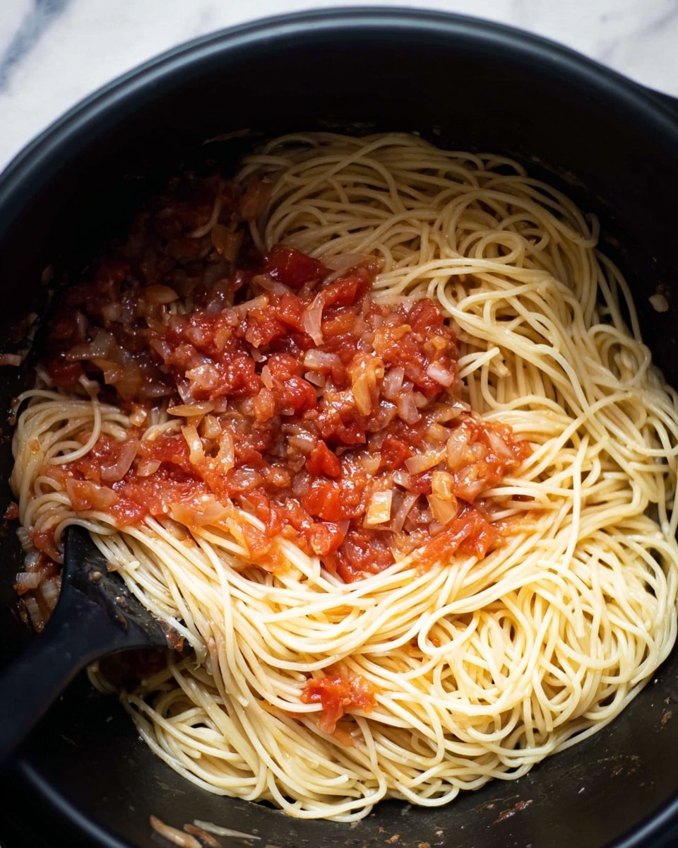 In a black pot, a dish of spaghetti is shown with a simple tomato sauce mixed in. There is one main layer of thin, light yellow spaghetti noodles topped unevenly with a chunky sauce made of small pieces of red tomatoes and hints of translucent cooked onion. The noodles have a smooth texture and are loosely piled, creating some loops and curves. A black utensil is partially visible in the bottom left corner, stirring the pasta and sauce. The background is a white marbled texture. photo taken with an iphone --ar 4:5 --v 7