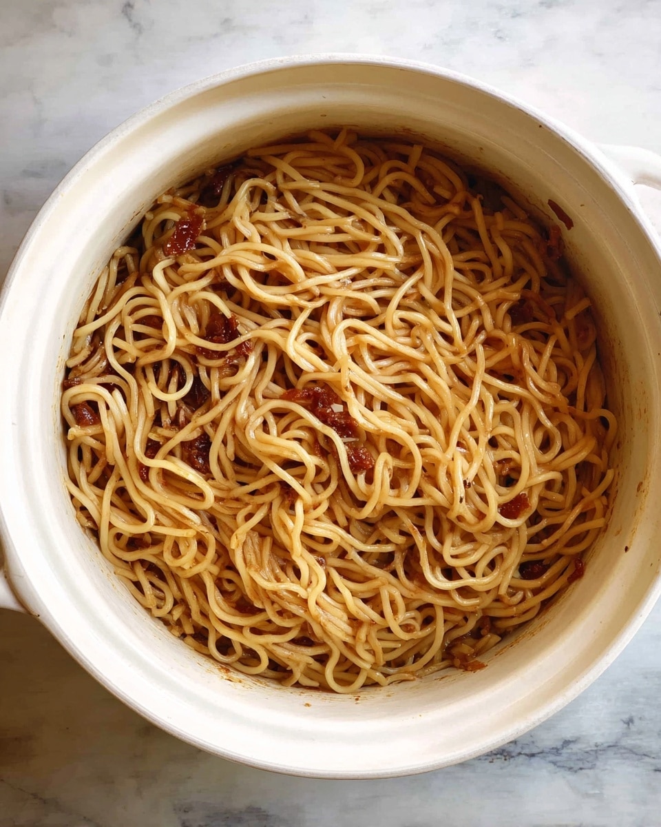 A white pot filled with light golden brown noodles arranged in a loose pile with some darker sauce coating parts of the noodles, small bits of darker brown and reddish pieces mixed evenly throughout, sitting on a white marbled surface. photo taken with an iphone --ar 4:5 --v 7
