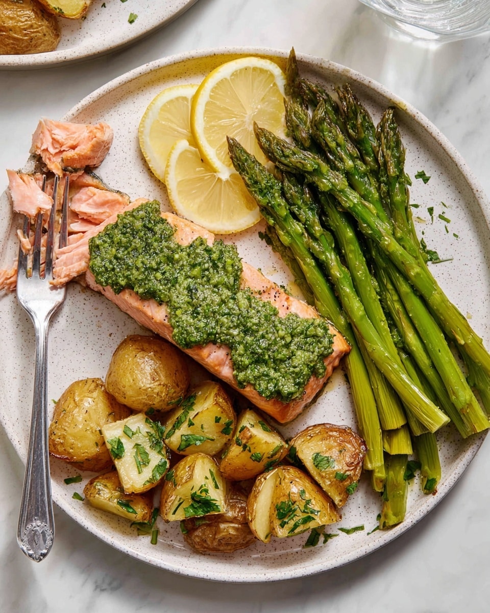 The image shows a white speckled round plate with three main parts: at the top left is a pink cooked salmon fillet topped with a bright green pesto sauce; a small piece of salmon is flaked off with a fork placed on the left side of the plate; to the right side, there are golden-brown roasted potato chunks with green herbs sprinkled on top; at the bottom of the plate, there is a group of bright green grilled asparagus spears arranged in a neat line. Two lemon wedges are placed on the left side of the salmon, and the plate sits on a white marbled surface. photo taken with an iphone --ar 4:5 --v 7