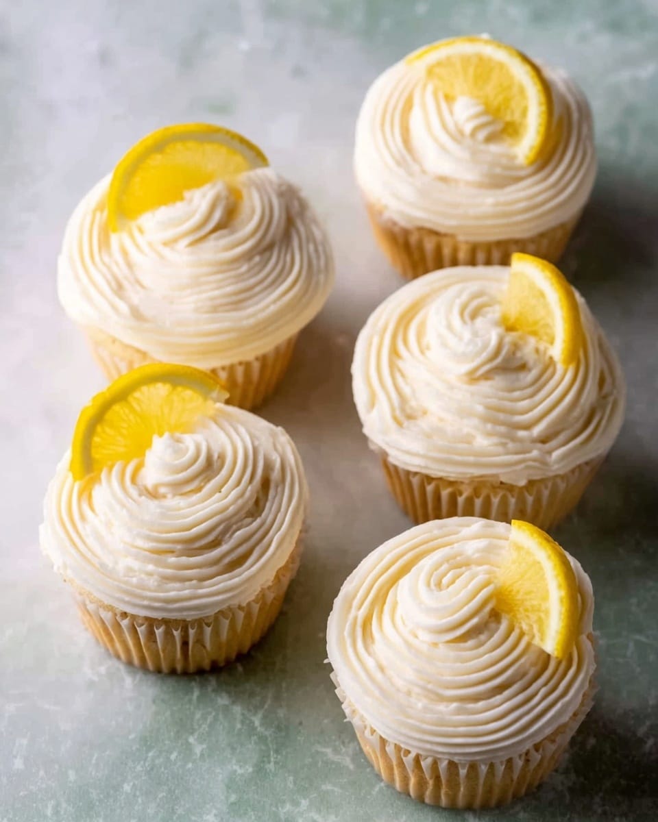 The image shows six lemon cupcakes arranged in rows, each topped with a swirl of smooth white icing that has fine ridges. On top of each cupcake, there is a small slice of bright yellow lemon placed slightly to the side, adding a fresh pop of color. The cupcakes sit on a white marbled surface, enhancing their bright and clean look. The texture of the icing looks soft and creamy, with the lemon slices giving a fresh citrus touch. Photo taken with an iphone --ar 4:5 --v 7