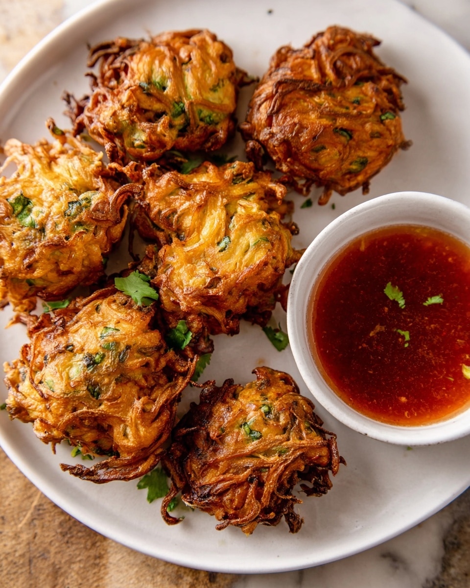 A white plate filled with seven golden-brown, crispy fritters that show curly, textured strands of fried onions and herbs inside. The fritters are sprinkled with small green herb pieces on top, adding a fresh touch. A small white bowl on the plate holds a shiny red dipping sauce with bits of herbs floating on the surface. The plate sits on a white marbled surface, and soft light highlights the crispy texture of the fritters and the smooth surface of the sauce. photo taken with an iphone --ar 4:5 --v 7