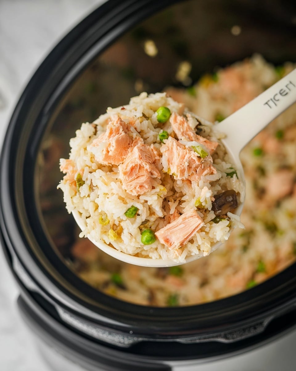 A close-up view of a white rice scoop holding a mix of cooked rice with chunks of light pink cooked salmon, scattered green peas, small pieces of green onions, and thin light brown mushrooms. The rice looks soft and slightly sticky, with the salmon pieces on top showing a flaky texture. The scoop is raised above a black rice cooker filled with the same rice mixture, softly blurred in the background. The whole scene is set on a white marbled surface. photo taken with an iphone --ar 4:5 --v 7