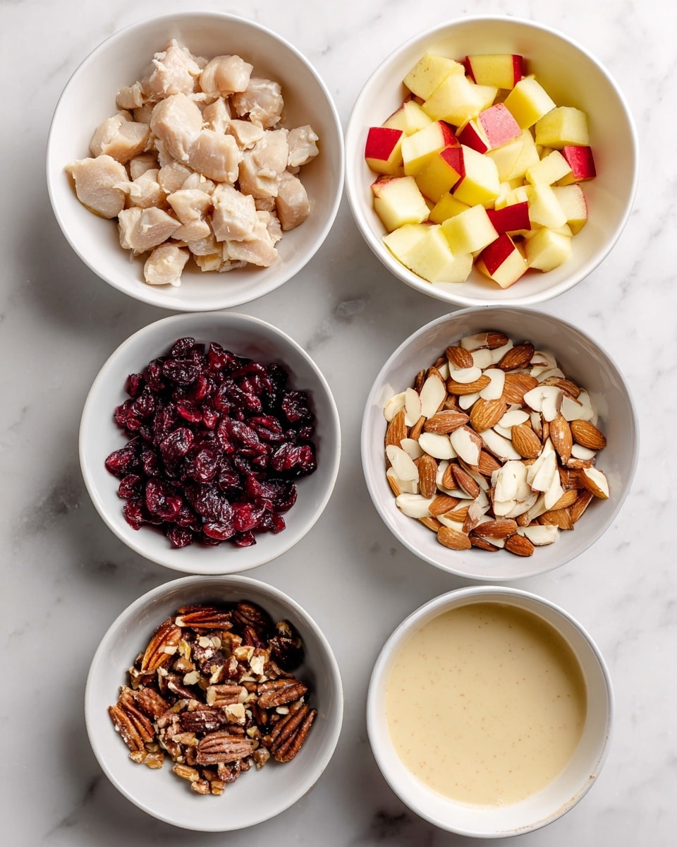 Five white bowls are arranged on a white marbled surface, each holding a different ingredient. The top left bowl is filled with small pieces of pale beige chicken. To the right, there is a bowl with small yellow and red diced apple pieces. In the center, there is a bowl of mixed sliced almonds with light and dark brown colors. The bottom left bowl contains dark red dried cranberries. The bottom right bowl holds a creamy light beige dressing. Each bowl's content is clearly visible. Photo taken with an iphone --ar 4:5 --v 7